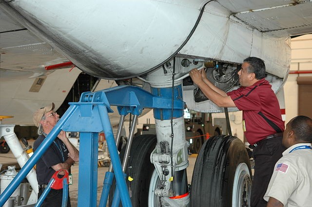 Technicians working on the undercarriage of a large aircraft